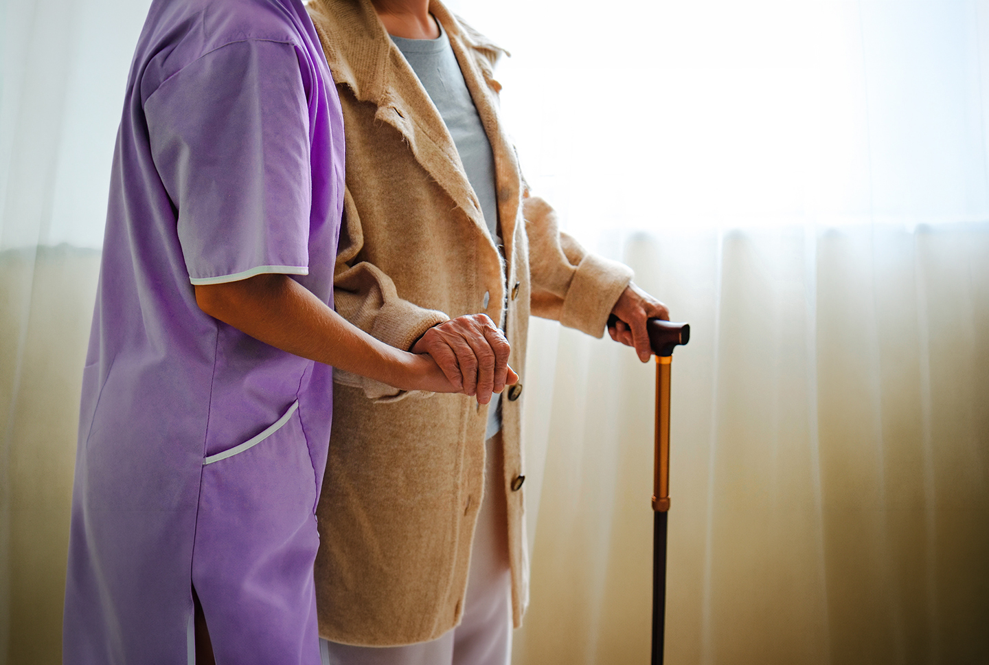 Caregiver assisting an elderly person with a cane.